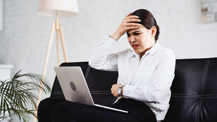 stressed businesswoman touching forehead while looking at laptop in office