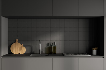 Front view close up of dark grey modern kitchen interior with kitchenware. Concrete floor. Black facades and ceramic tiles on wall