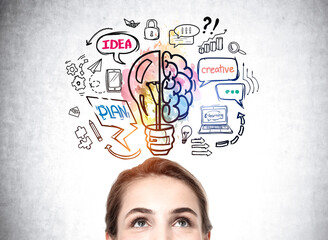 Half portrait of businesswoman looking up at colorful lightbulb and brain sketch on concrete wall....