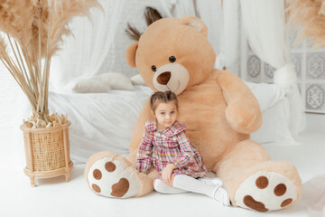 Cute charming little girl in a dress with soft toys, in a light photo studio. Teddy bears and hares.