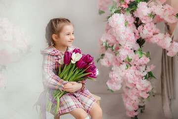 Cute adorable little girl in a dress holding a bouquet of tulip flowers, in a bright photo studio.