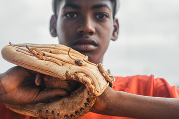 boy with brown skin and latin origin playing baseball in the park with ball, glove and bat, dark...