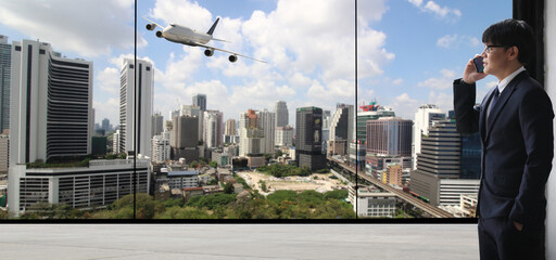 Full length rear view of a young stylish businessman standing at the large windows of a high office, looking at the view of a harbor below,logistics or transportation concept