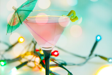 pink cosmopolitan cocktail with lemon peel and colourful string lights