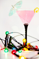 pink cosmopolitan cocktail with lemon peel and colourful string lights