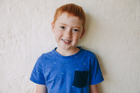 Portrait of a young red haired boy smiling in a blue shirt