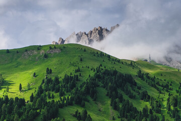 A green hill with a rocky peak and clouds in the background