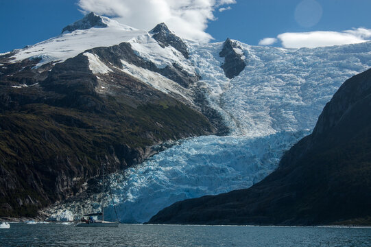 A sailboat floats in front of huge glaciers leaping into the sea