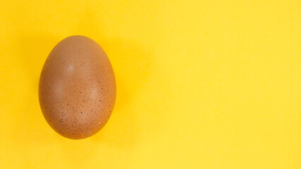 One chicken raw egg on yellow background. Farm products. Easter concept with copy space.