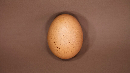One raw egg on a brown background. Copy space. Minimal concept. 