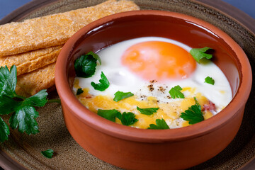 Egg en cocotte with cheese in the ceramic portion bowl served with parsley and whole grain crispbread. French food