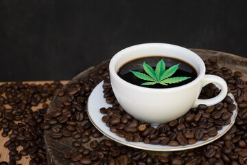 Coffee cups, coffee beans and cannabis leaves on black background The concept of drinking coffee with herbal ingredients, cannabis leaves, is legally licensed by law.