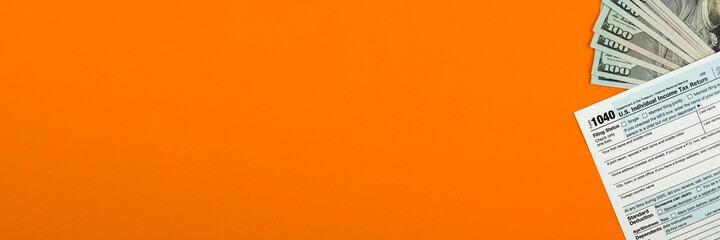 Naklejka premium US individual Income Tax Form 1040 with dollar bills on the desktop, orange background with copy space