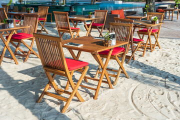 Fototapeta na wymiar Wooden table and chairs in empty beach cafe next to sea. Close up, Thailand