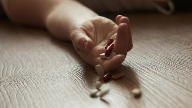 Woman lying unconscious on the floor with capsules in her hand. Close-up.