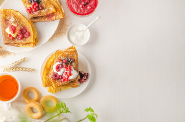 Pancakes with berries, sour cream and tea for the Maslenitsa on a white plate with copy space