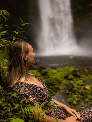 Young Caucasian woman enjoying waterfall landscape in tropical forest. Woman portrait. Energy of water. Travel lifestyle. Nung Nung waterfall, Bali