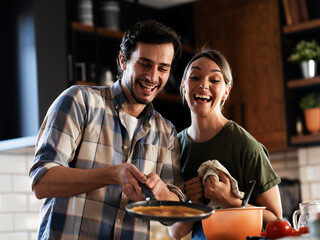 Boyfriend and girlfriend making pancakes at home. Young couple having fun in the kitchen