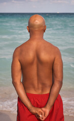 Man from behind in red short pants. He looks at the sea.
