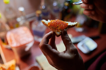 Man making red caviar sandwich with creamy cheese. Closeup lowlight photo. Russian cuisine.