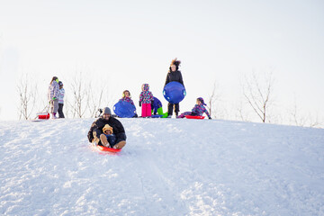 Cute child happily riding down a hill on a toboggan sled with his dad. Interracial family