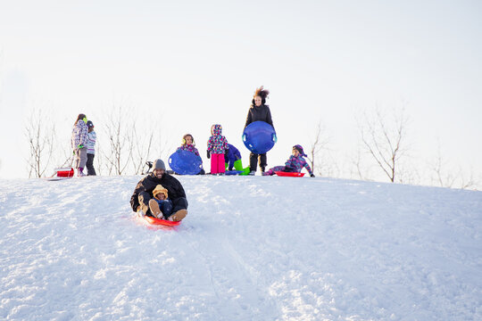Cute child happily riding down a hill on a toboggan sled with his dad. Interracial family