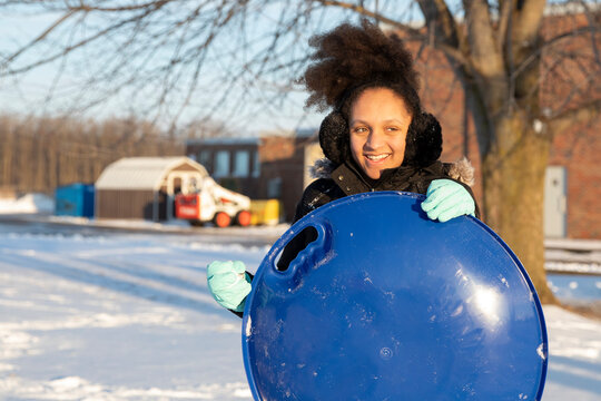 A teen girl having a snowball fight with her sister and using a sled as a shield.