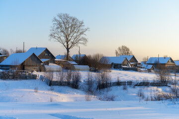 Obraz premium View of the Ural (Russia) village - the Russian hinterland in winter. Mountainous area with tall trees. Traditional style wooden houses with vegetable gardens, sheds and greenhouses in the snow