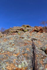 Weathered Lichen Covered Sheer Rock on Top of Cliff against Blue Sky 