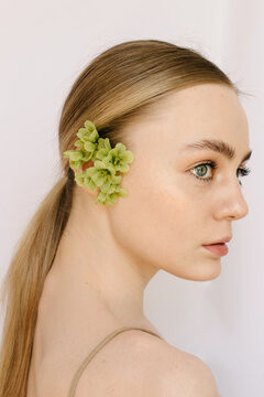 Sensual portrait of a young blond girl with little flowers in her ear