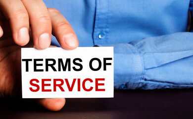 TERMS OF SERVICE is written on a white business card in a man's hand. Advertising concept