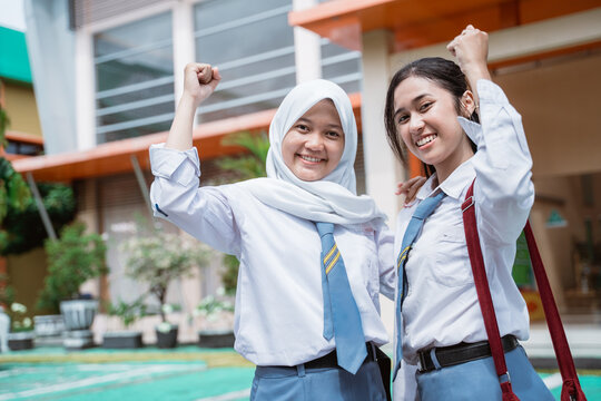 Close Up Of Two Beautiful Student Wearing An Indonesian High School Uniform And Bag With Raise Hands When Standing Against The Background Of The School Building.