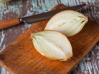 Onions cut into halves on a kitchen board and a kitchen knife