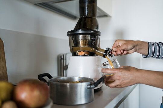 Woman preparing fresh juice for breakfast at home, using a centrifuge