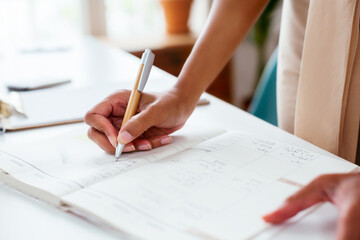 Crop ethnic entrepreneur writing in planner