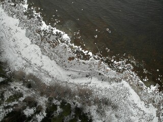 Winter shore of lake with stones and forest. Ice snow. Aerial voew from top down