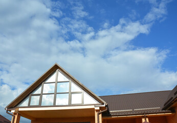 A modern house with an attic panoramic triangular window or attic skylight glass, window wall and metal roof with snow guards.