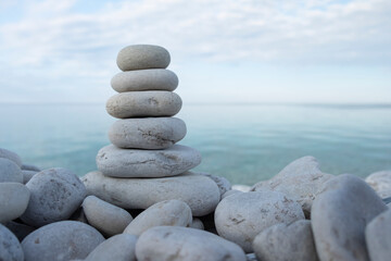 Flat rocks stacked on top of each other standing vertically on the beach, blue water and sky out of focus in the background, soft light. Balance, harmony, relaxation and peace concept. Space for copy.