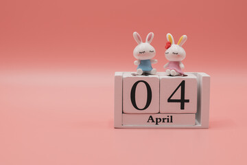 Wooden calendar, April 4th. Day 4 of month and two cute rabbits on sweet pink background,...