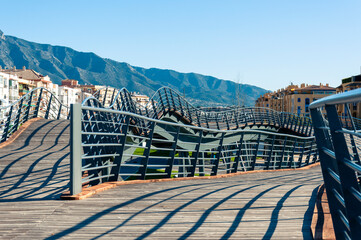 Curved, wooden-paved, metal-fenced footpaths stand on poles, residential buildings to the left and right, and a mountain range in the background