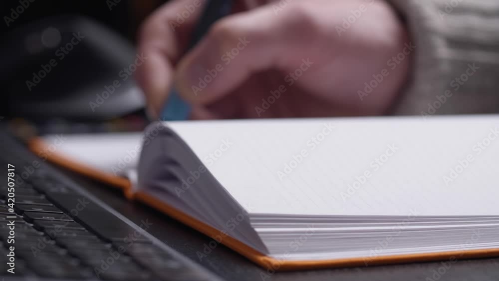 Poster hand writing in notebook, keyboard from a side perspective with blurred background.