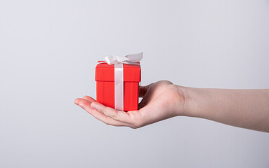 Women's hands hold a red holiday gift box with a white ribbon