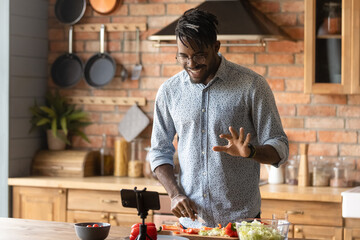 Cooking master class. Confident black man vlogger shoot tutorial teach audience to make healthy food. Young african guy capable cook broadcast live preparing national cuisine dish on domestic kitchen - obrazy, fototapety, plakaty