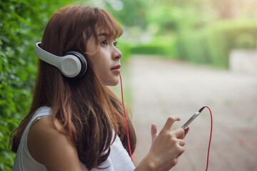 Image of young Asian woman wearing headphone to listen to music in exercise in the park