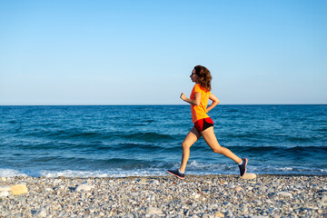 Fototapeta na wymiar A slender woman in a bright orange T-shirt runs along the beach.