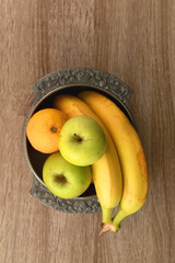 Antique bowl with bananas, apples and lemons on wooden table. Top view.