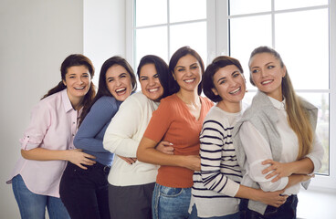 Group portrait of happy young women. Team of female friends or office coworkers in their 20s and 30s standing close together, smiling and looking at camera. Concept of unity and supporting each other