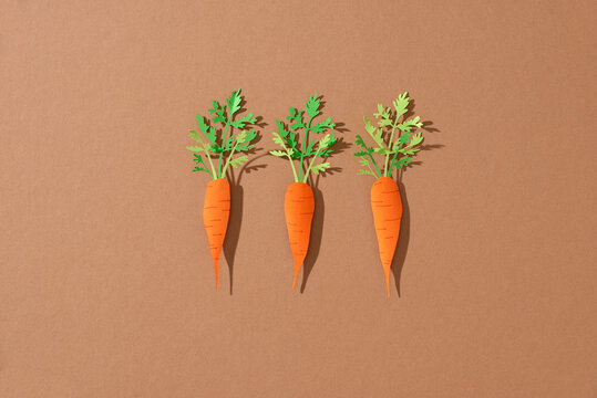 Three carrots make from paper on brown background