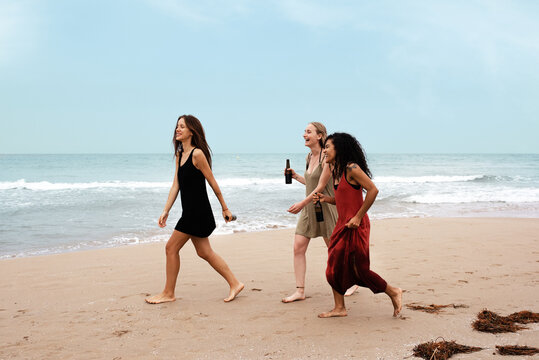 Happy diverse friends with beer walking near sea