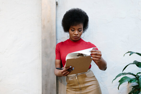 Attractive restaurant manager leaning on white wall checking a folder